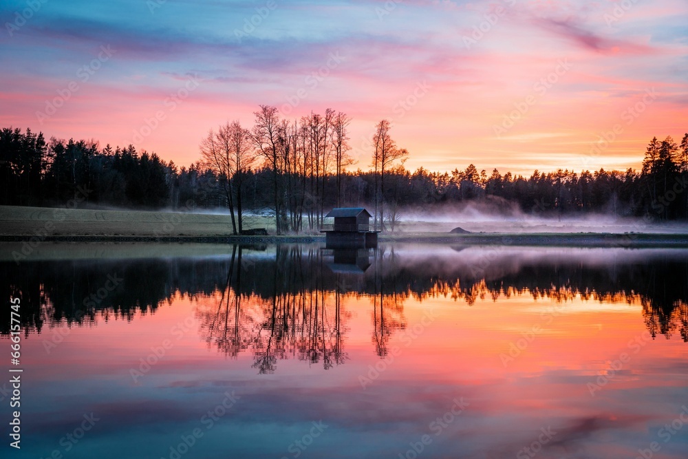 a lake at sunset reflecting a forest surrounding it with mist