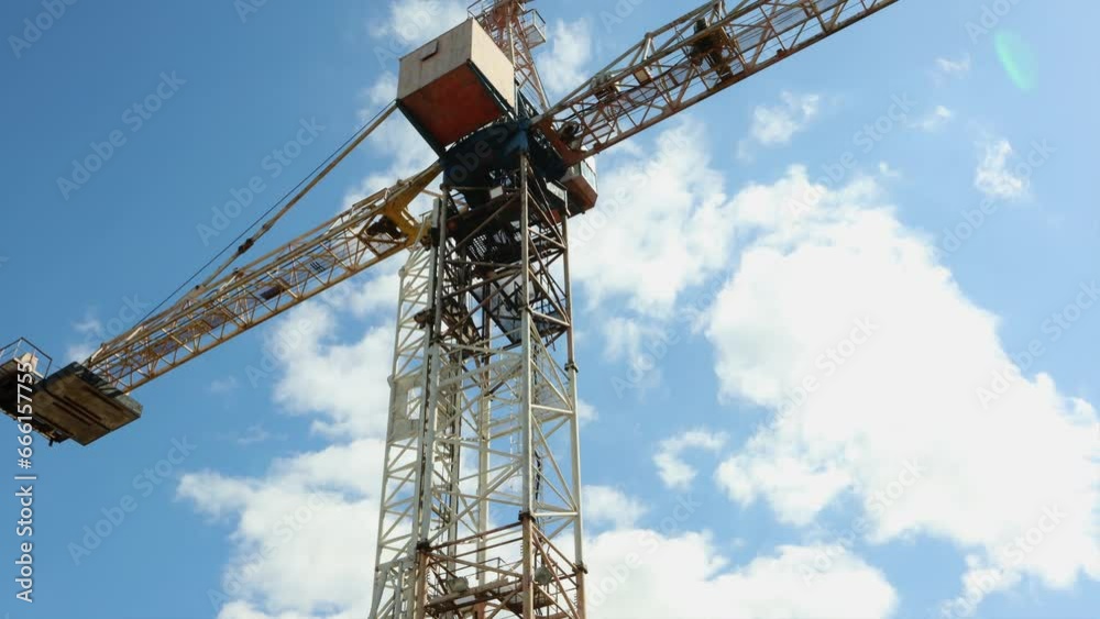 Large construction crane against a background of blue sky with clouds, time lapse of the sky during the day in the bright sun Large construction crane against a background of blue sky with clouds, time lapse of the sky during the day in the bright sun