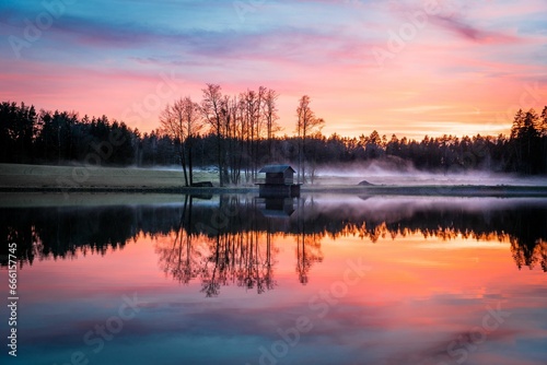 a lake at sunset reflecting a forest surrounding it with mist © Wirestock