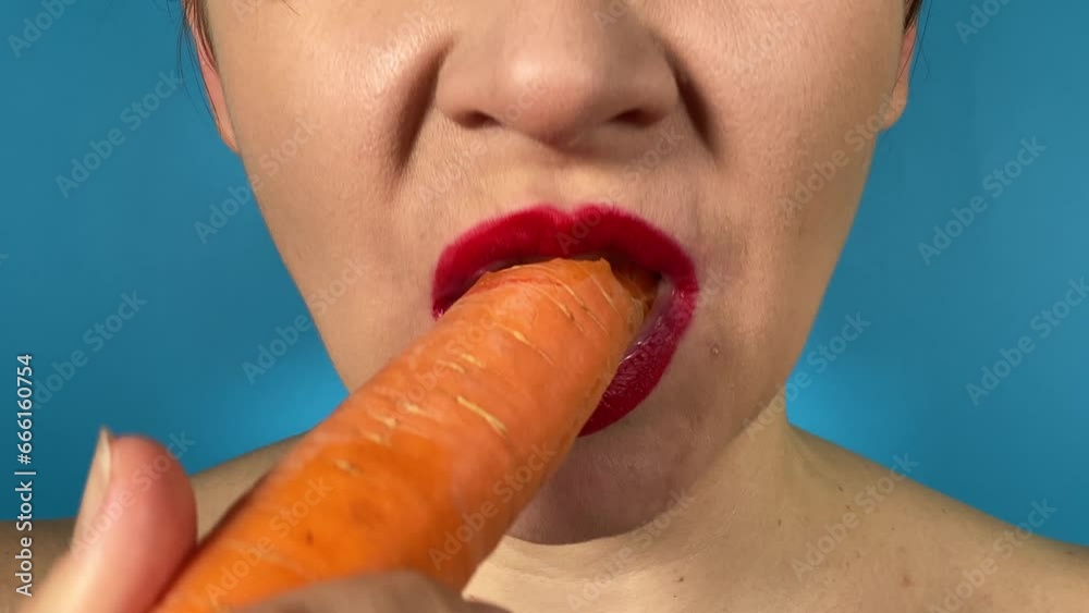 Young woman vibrantly colored lips enjoys healthy snack, biting fresh carrot, savoring every crunchy moment indoors. Close-up mouth red lipstick tasting root vegetable isolated on blue background Young woman vibrantly colored lips enjoys healthy snack, biting fresh carrot, savoring every crunchy moment indoors. Close-up mouth red lipstick tasting root vegetable isolated on blue background
