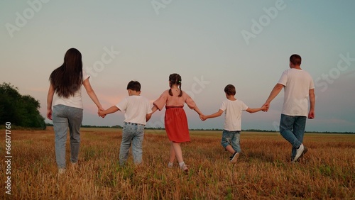 Big family, group of people in nature. Happy family with children walks in grass field in summer. Dad mom daughter son go hand in hand outdoors in autumn. Parental care for children. Active family