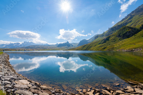 Sun and Clouds are reflecting in the clear water of a mountain lake. Melchsee-Frutt near Lucerne, Switzerland in the Swiss Alps. Serene Lake Landscape in summer.