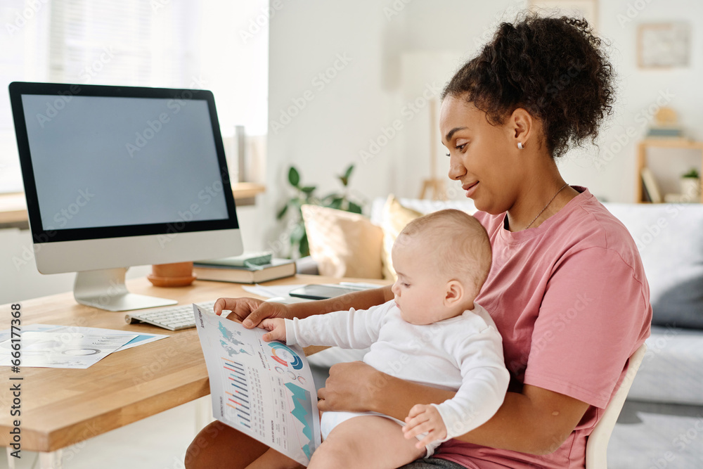 Young woman working with financial graphs while sitting at home with her baby Young woman working with financial graphs while sitting at home with her baby