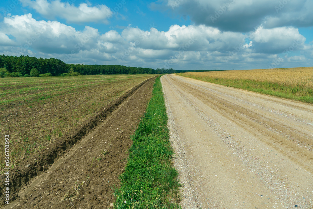 A dry sandy road passes through a field under the scorching sun and clouds. Dirt road outside the city in the village. Arid climate on earth. Climate change and its consequences. A dry sandy road passes through a field under the scorching sun and clouds. Dirt road outside the city in the village. Arid climate on earth. Climate change and its consequences.