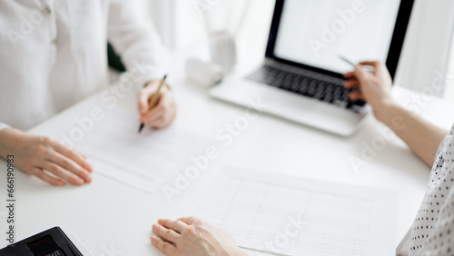 Two accountants using a laptop computer for counting taxes at white desk in office. Business Woman pointing into screen with a pen. Teamwork in business audit and finance