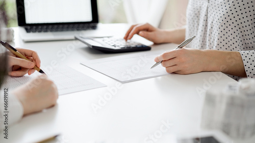 Two accountants using a calculator and laptop computer for counting taxes or revenue balance while rolls of receipts are waiting to be calculating. Business audit and taxes concepts