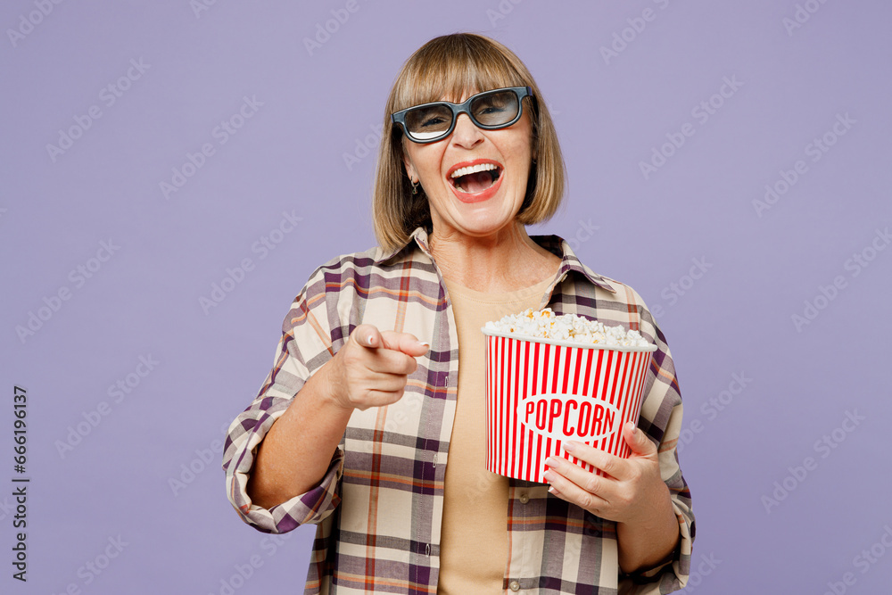 Elderly woman in 3d glasses 50s year old in beige t-shirt shirt casual clothes watch movie film hold bucket of popcorn in cinema point finger camera on you isolated on plain purple background studio Elderly woman in 3d glasses 50s year old in beige t-shirt shirt casual clothes watch movie film hold bucket of popcorn in cinema point finger camera on you isolated on plain purple background studio