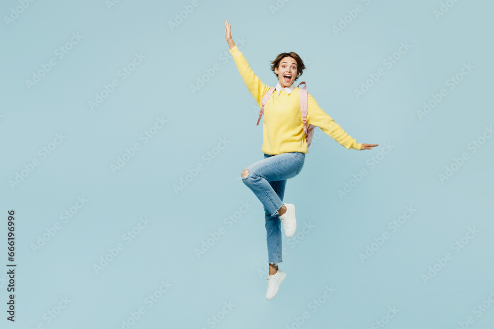 Full body young excited woman student wear casual clothes sweater hold backpack bag stand on one leg with outstretched hands isolated on plain blue background. High school university college concept.