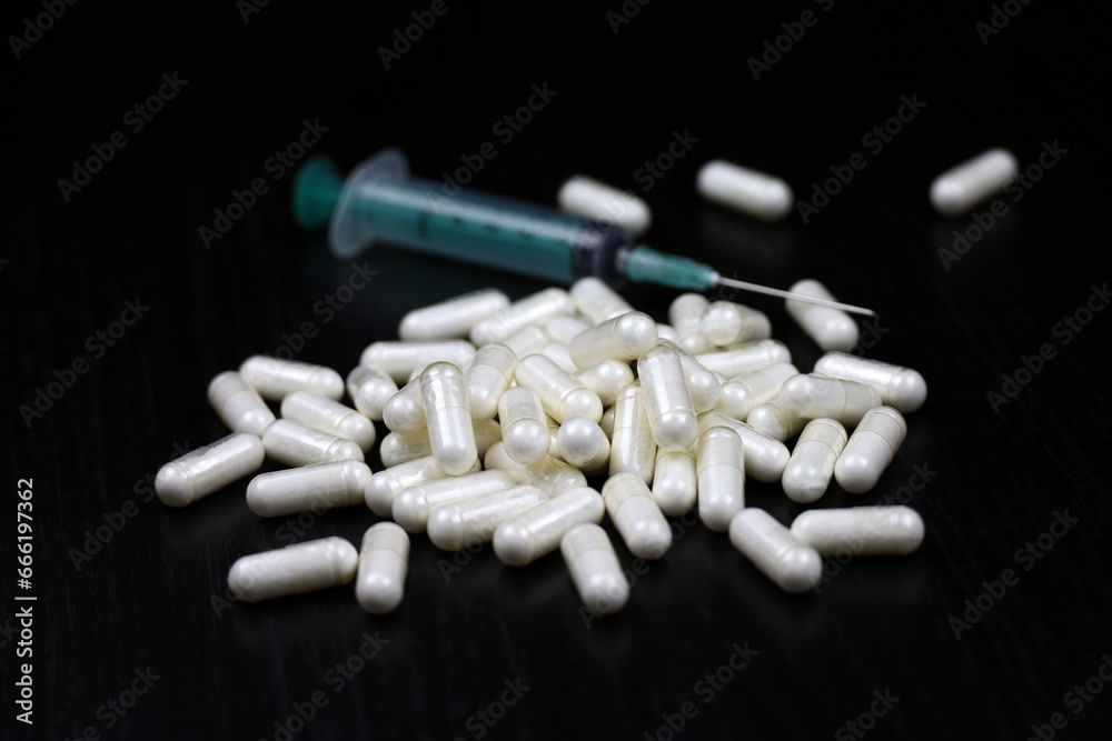 White pills and syringe on a black wooden table, medication in capsules. Background for pharmacy, antibiotics, vitamins White pills and syringe on a black wooden table, medication in capsules. Background for pharmacy, antibiotics, vitamins