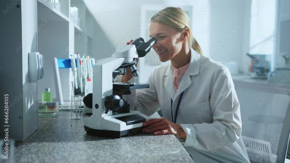 Smiling scientist woman looking under the microscope worker in the laboratory. Medicine, biotechnology research. Pharmacology Smiling scientist woman looking under the microscope worker in the laboratory. Medicine, biotechnology research. Pharmacology
