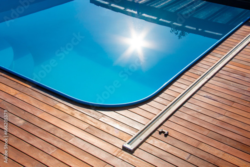 Ipe wood decking around the pool, edge of the outdoor swimming pool with sun reflection on the blue water