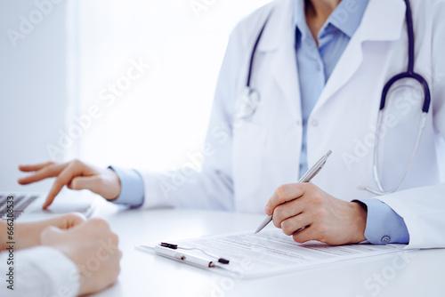 Doctor and patient discussing something and using laptop while sitting opposite each other at the desk in clinic office. Perfect medical service and medicine concept