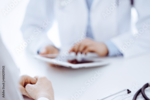 Stethoscope lying on the tablet computer in front of a doctor and patient sitting opposite each other and using tablet computer at the background . Medicine  healthcare concept
