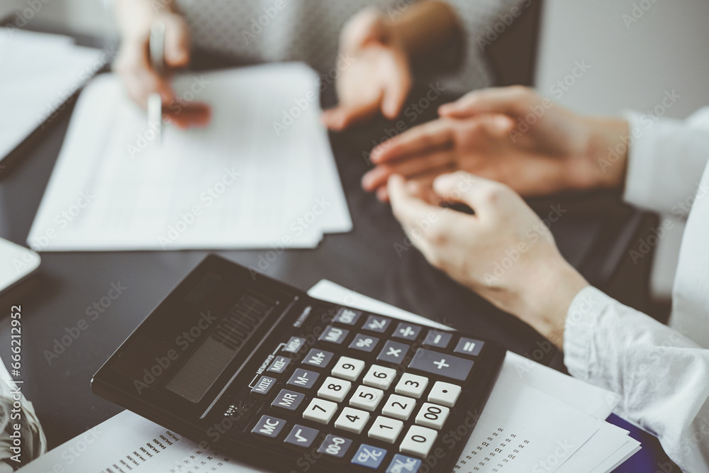 Woman accountant using a pen and laptop computer while counting and discussing taxes with a client, focus on the calculator. Business audit and finance concepts Woman accountant using a pen and laptop computer while counting and discussing taxes with a client, focus on the calculator. Business audit and finance concepts