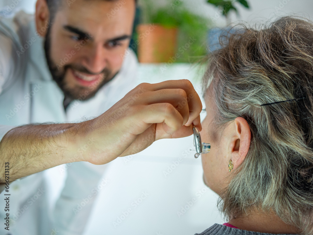 Fototapeta premium Young audiologist helping to insert an electronic hearing aid to an old woman patient