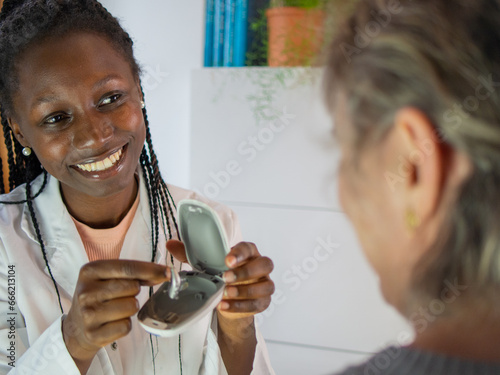 Young female audiologist helping to insert an electronic hearing aid to an old woman patient photo