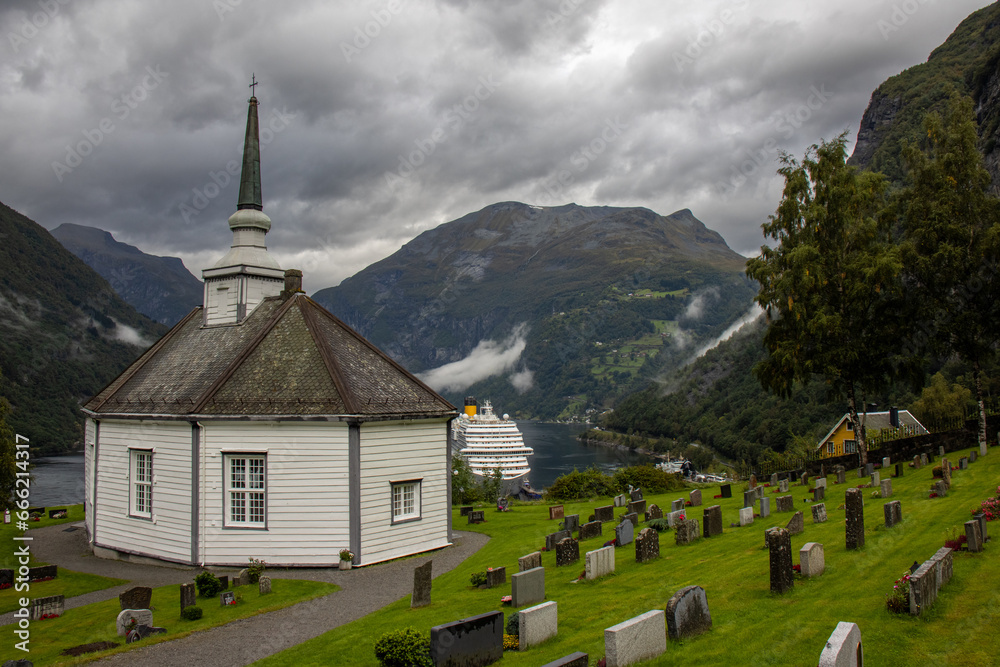 The beautiful octagonal Geiranger church next to the cemetery. It is made of white wood with a black slate roof. It has spectacular views of the Geiranger Fjord and the mountains, Norway