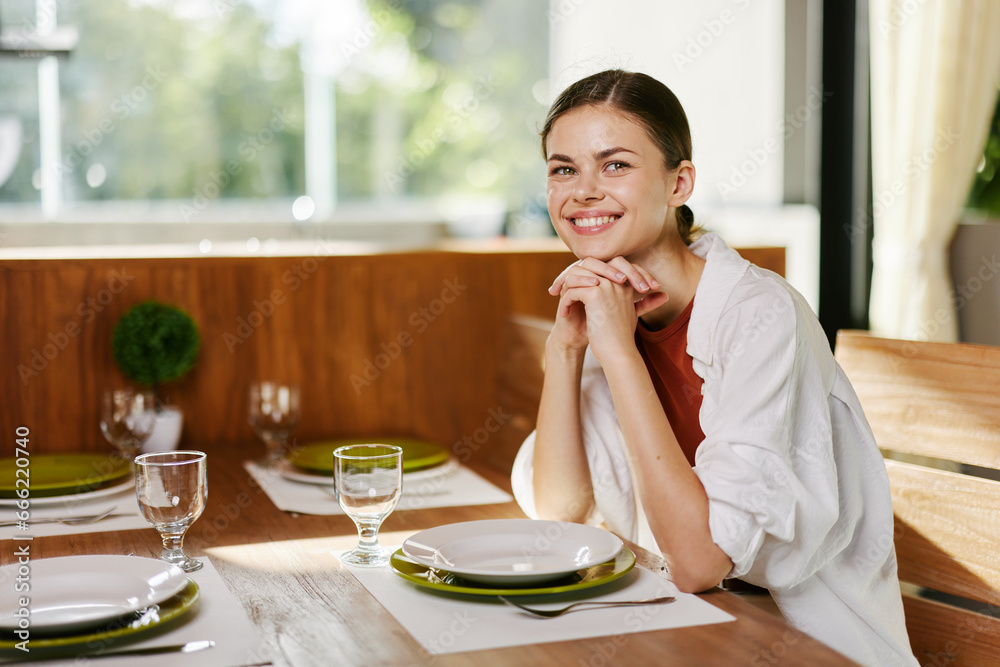Stylish woman sitting at dining table drinking water from a glass, home modern interior, sunset light, lifestyle in comfort. Stylish woman sitting at dining table drinking water from a glass, home modern interior, sunset light, lifestyle in comfort.