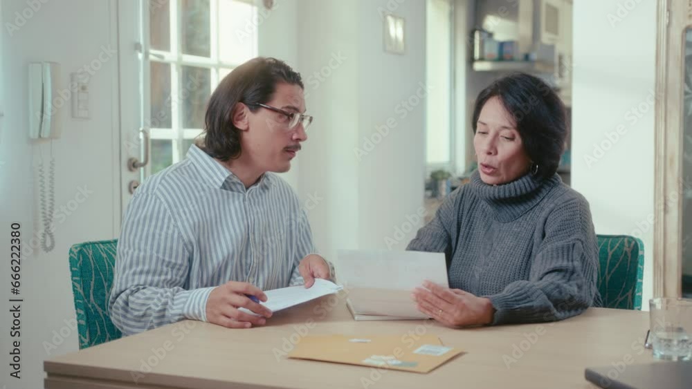 Insurance agent and mature Hispanic woman sitting at table in the living room and discussing documents during at-home consultation Insurance agent and mature Hispanic woman sitting at table in the living room and discussing documents during at-home consultation