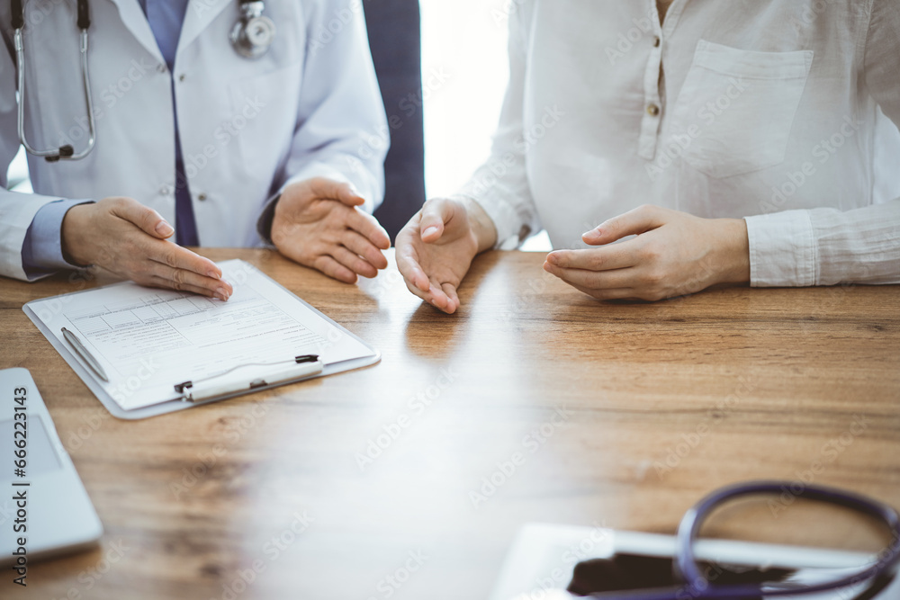 Doctor and patient discussing something while sitting near each other at the wooden desk in clinic, view from above. Medicine concept