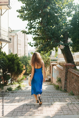 A slender girl with long hair in a blue dress walks along the street among the old buildings of the ancient city.A beautiful woman in an evening dress posing against the background of old architecture