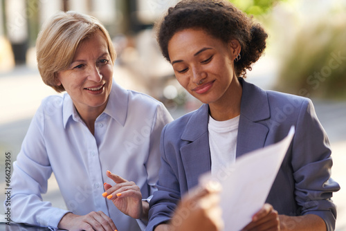 Two smiling business coleagues working with documents sitting outdoors of office photo