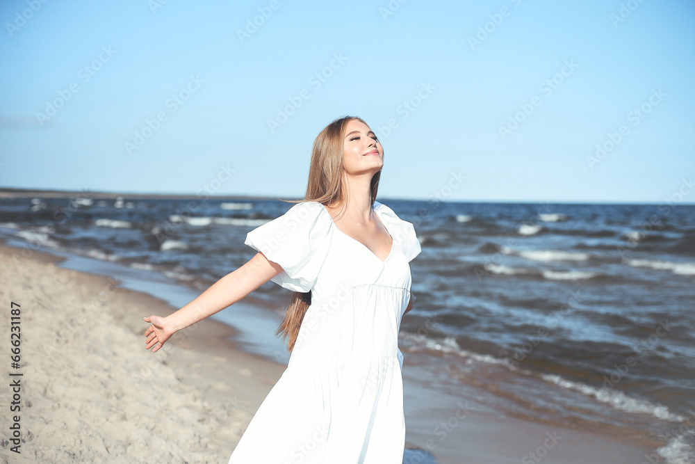 Happy smiling beautiful woman is on the ocean beach in a white summer dress, open arms Happy smiling beautiful woman is on the ocean beach in a white summer dress, open arms