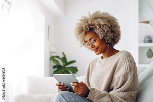 Happy mature black woman using tablet on white wall in smart home. Modern home innovation and technology. Using a mobile tablet to control smart home photo