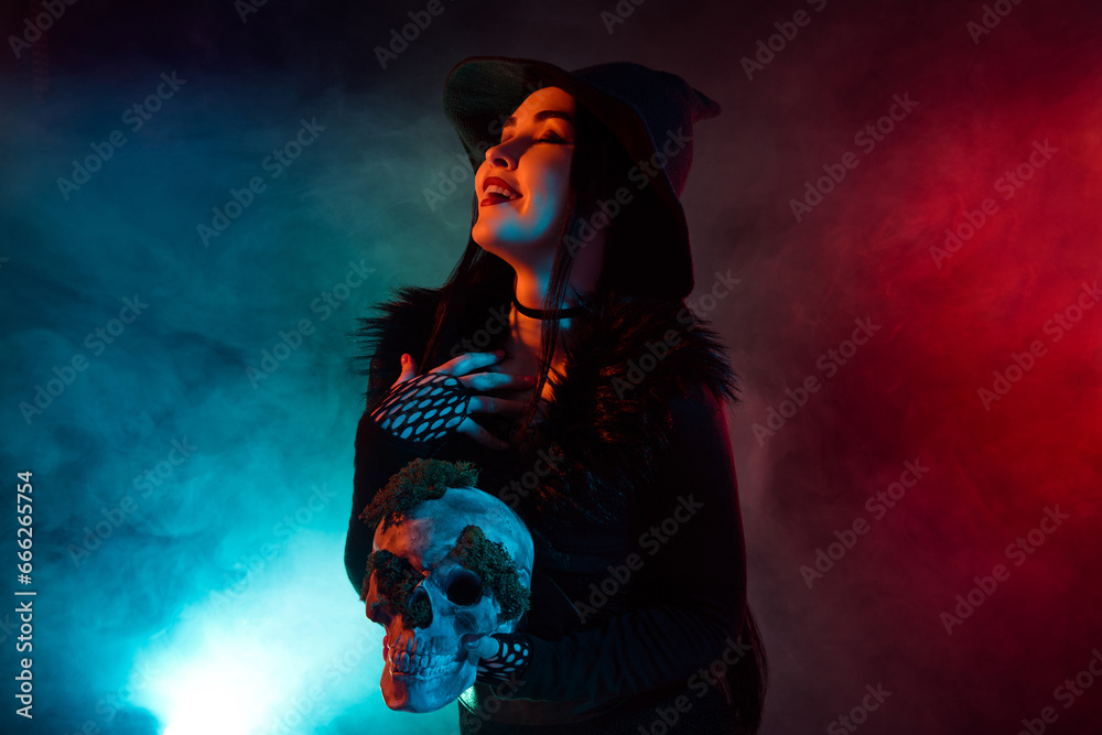 Photo of dangerous goth witch lady hold skull ingredient to potion for summon dark devil over mist background