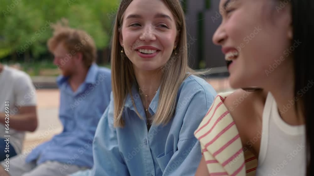 Group of laughing multinational young students talking on the bench near university in summertime Group of laughing multinational young students talking on the bench near university in summertime