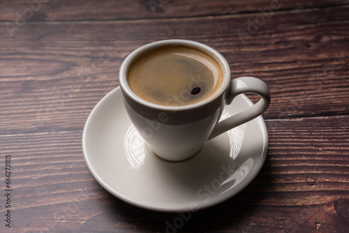 Close up of espresso coffee in white cup, on wooden background with shadowplay , vintage color tone, 
