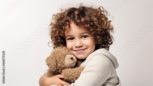 smiling curly Child hugging plush teddy bear on beige background with copy space. cute adorable kid embrace teddy bear. photo
