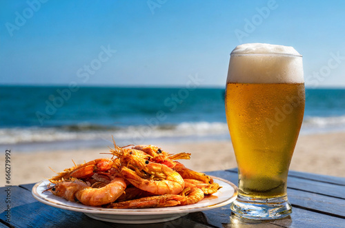 A glass of beer and a portion of fried prawns on a table at the beach