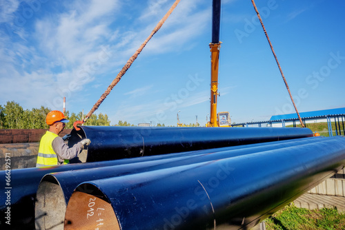 Slinger unloads large gasification pipes on summer day. Pipes for transporting natural gas. Construction of gas pipeline. Storage of large diameter metal pipes.