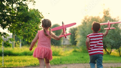 Child, boy, girl play in park, friends run together, dream of flying. Children play run fly with toy plane in sky. Airplane imagination of children, concept of active play in nature. Holiday family.