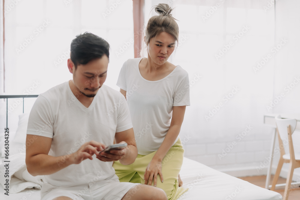 Fototapeta premium Funny asian couple. Wife peeking husband who chatting on the smartphone.