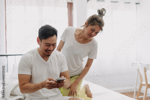 Funny asian couple. Wife peeking husband who chatting on the smartphone.