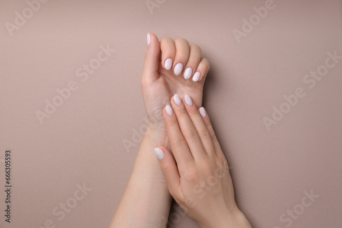 Woman showing her manicured hands with white nail polish on light brown background  top view