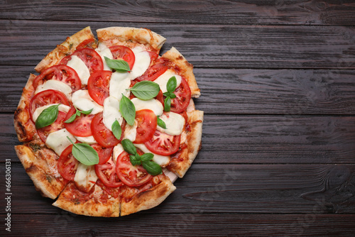 Delicious Caprese pizza with tomatoes, mozzarella and basil on dark wooden table, top view. Space for text