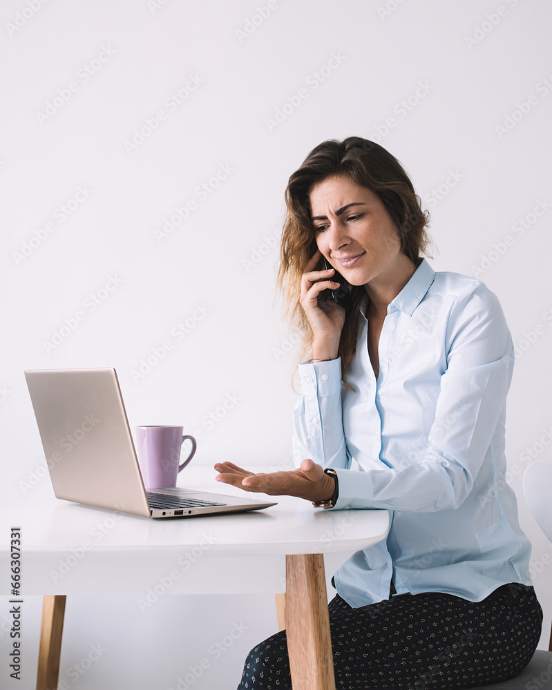 Confused woman talking on phone and watching laptop Confused woman talking on phone and watching laptop