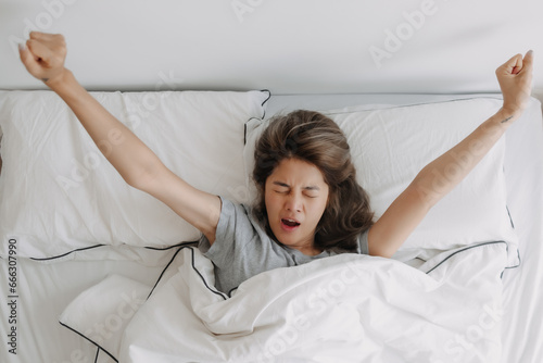 Top view of yawning and stretching asian woman just wake up on the bed.