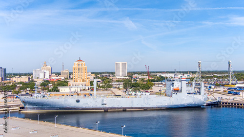 Aerial view of Beaumont Texas cityscape with modern and historic building, a large  Fuel storage tanks, the Commercial Dock and Port and oil refineries in the background with a partly cloudy blue sky.