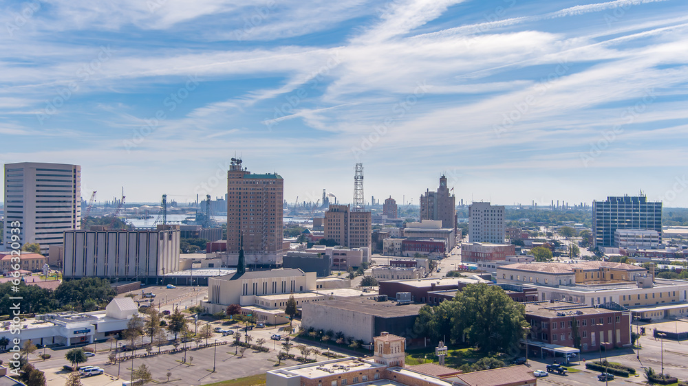 Aerial view of Beaumont Texas cityscape with modern and historic building, Fuel storage tanks, the Commercial Dock and Port and oil refineries in the background with a partly cloudy blue sky.