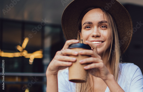 Joyful trendy woman drinking coffee while reading book in cafe