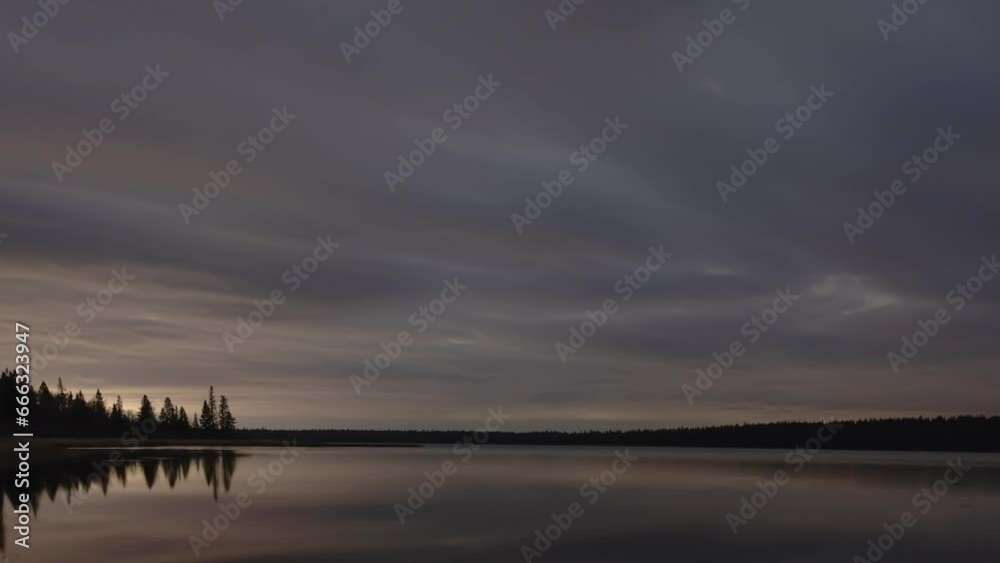 Moody gray clouds move through the night sky above a calm northern lake ...