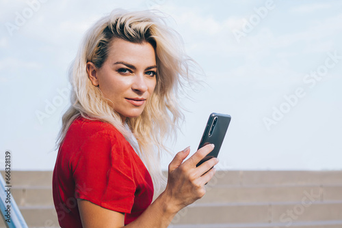 Confident woman with smartphone looking at camera on stairs
