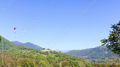 Paragliding Flying over Mountain Village Breno on Mountain Peak in a Sunny Summer Day in Breno, Malcantone, Ticino, Switzerland, Europe photo