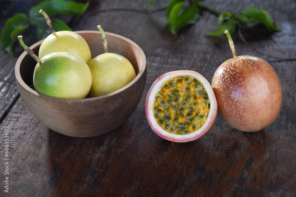 Passion fruit (Maracuya) in a bamboo tray and cut in half with green leaves on a wooden table background.