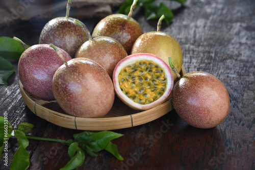Passion fruit (Maracuya) in a bamboo tray and cut in half with green leaves on a wooden table background.
