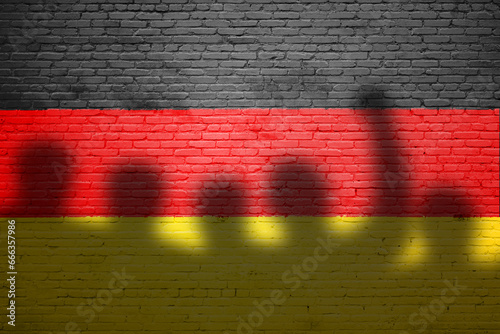 The refugees migrate to Germany . Silhouette of illegal immigrants . Europe union migration policy. Germany flag painted on a brick wall with protesters photo